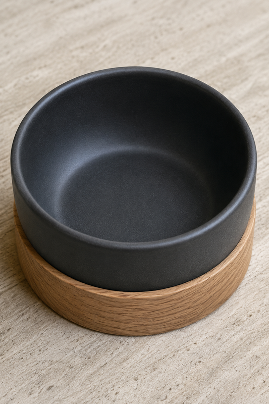 Matte black ceramic bowl in a solid oak base on a pale stone surface