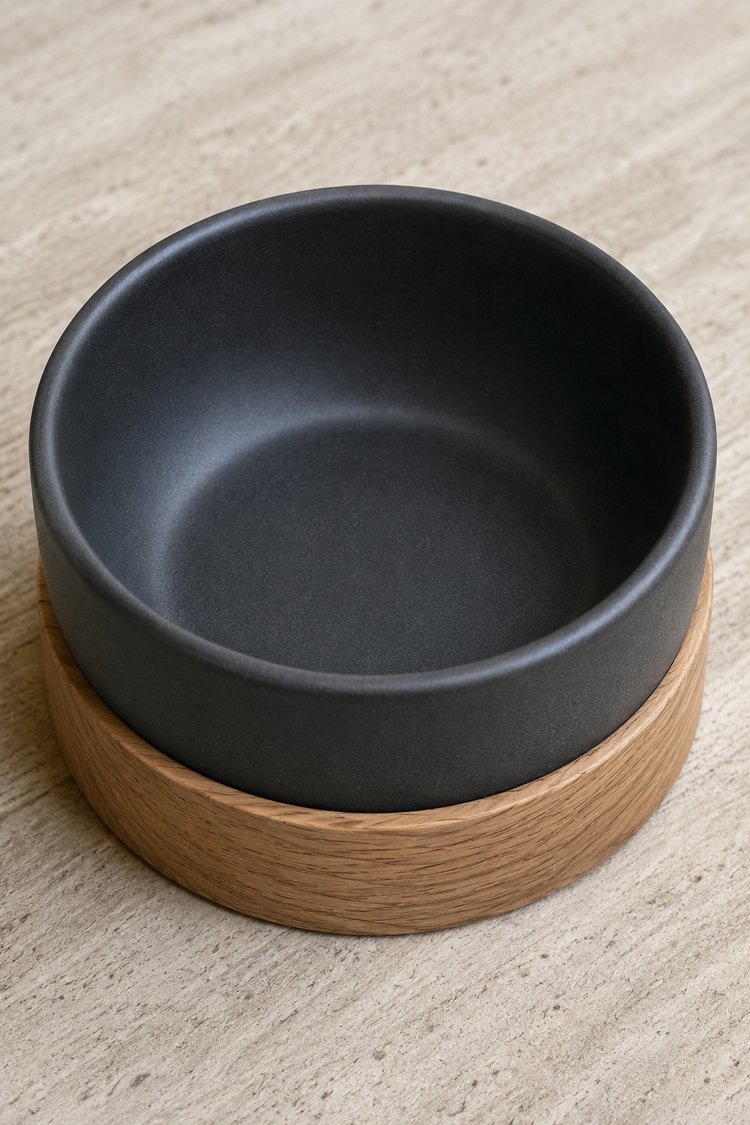 Matte black ceramic bowl in a solid oak base on a pale stone surface